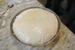 And then carefully tucks the overhanging layers down the inside edges of the pan, sealing the bisteeya. A final brush with clarified butter is added to the top so it shines.