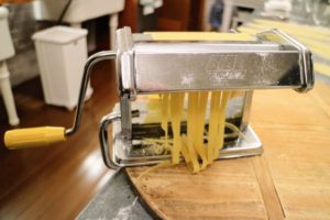 After the dough rectangles are rolled through the pasta machine set at its widest openings and then through progressively narrower settings, it is fed through the attachment to form fettuccine strips.
