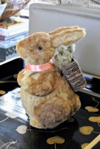 An antique rabbit with backpack sits on a black lacquered side table.