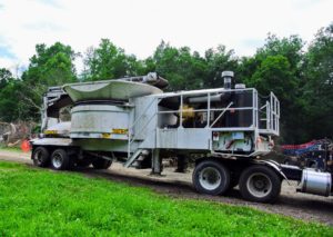 The tub grinder is moved into position in front of the large wood pile. Tub grinders are typically loaded from the top by the excavator.