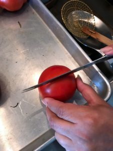 Working in batches by color, Enma scores a shallow “x” on each tomato. Here she is making the first cut.