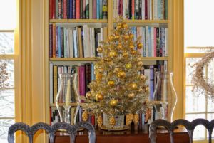 I love this tabletop tree, flanked by candles in front of this bookcase. It's decorated with gold balls and ornaments shaped like pinecones.