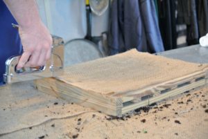 Once the burlap was cut to the appropriate measurements, using a stable gun, Ryan affixes the burlap to the back of the frame.