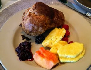 This plate includes a warm popover, fresh fruits and jam.