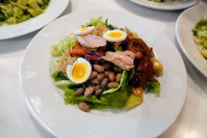 Salade niçoise originated in the French city of Nice. It is traditionally made of tomatoes, hard-boiled eggs, Niçoise olives, anchovies, and dressed with olive oil.