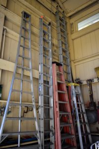 Ladders of various sizes rest against one wall above the wheelbarrows and close to one set of large barn doors for easy access.