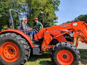 Here I am in the driver's seat - ready to mow the hayfield. My outdoor grounds crew foreman, Chhiring, is at my side giving me some direction on the new equipment. The turbocharged four-cylinder engine is designed to reduce noise and vibration, so we can communicate while it moves.