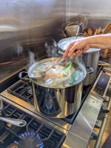 And he adds the onions and many of the cut vegetables to the pots for a more flavorful broth. He also continues to remove any fat at the top until the broth is as clear as possible.
