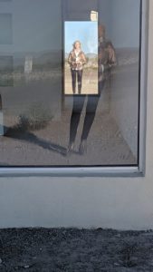 Here I am standing in the doorway, which is nonfunctional. I loved the reflection in this photo. The building is made of adobe bricks, plaster, paint, glass pane, aluminum frame, MDF, and carpet.