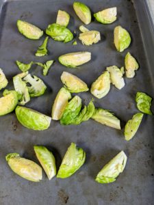 She trims and cuts the Brussels sprouts, tosses them with oil and vinegar, and places them on a rimmed baking sheet for roasting.