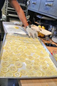 Slices of lemon are placed on a lined cookie sheet. Each slice is about one-eighth of an inch thick.