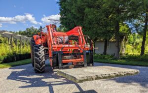 These caps are extremely heavy, so Chhiring uses our trusted Kubota model M7060HD12 tractor in the signature bright orange color with the pallet fork attachment to carefully remove the bluestone cap from the basin opening.