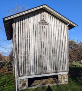 This is the outside of the corn crib. This structure is original to the farm. A corn crib is a type of granary used to dry and store corn. It may also be known as a corn house. The basic corn crib consists of a roofed bin elevated on posts. Another typical early American design has walls slanted outward.