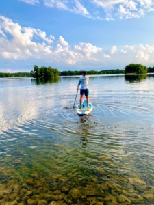 To use a paddle board, it is important to first get out into in water so the fins are free from hitting the bottom. Garrett takes a few strokes on each side of the board while maintaining a steady stance in the middle. His feet are parallel to the stringer – about shoulder width apart. And he keeps a slight bend in the knees and his core centered over the board.