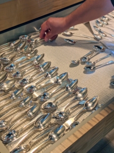 Enma carefully returns the spoons back inside the drawer, lining them up with other like pieces.
