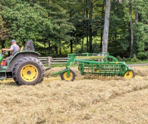 The hay rake is pulled at a slight angle to the tractor as it moves.