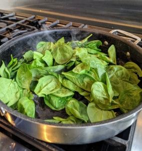 The spinach is cooked in a large pan with olive oil, salt, and pepper until just slightly wilted.