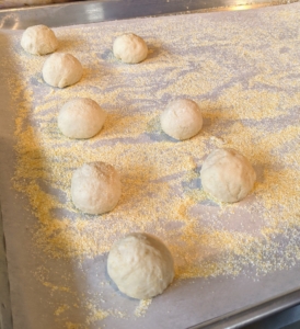 Each piece is shaped into a ball, placed on a parchment paper-lined sheet pan and then sprinkled with cornmeal.