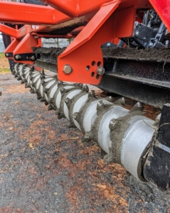 Here is a closer look at the roller of the power rake. When it is lowered onto the road surface and tilted to the proper angle, this attachment moves the gravel and road dust to the center, creating the proper crown for the surface. There should be about a three-percent slope from the shoulder to the center of the 12-foot wide road.