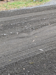 In this section of the road, there is a small pothole, or a depression in the surface, where traffic and water have removed the gravel.