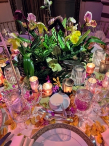 This lovely centerpiece featuring orchid flowers, their bold foliage, and petals all around the table is by Dorothy Pfieffer of Cornucopia.
