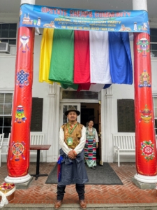 Chapter president, Chhiring Sherpa, dressed in his traditional Sherpa formalwear. Behind him is his wife, Ang Pema. Above are Tibetan prayer flags - each hue signifies an element — and the flags are always arranged in a specific order of yellow, green, red, white and blue. Blue represents the sky, white represents the air, red symbolizes fire, green symbolizes water, and yellow symbolizes earth. All five colors together signify balance.