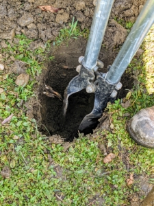 Here’s a closer look at the post hole digger – this tool is available at any hardware store. A post hole digger is also known as a clamshell digger, because of its resemblance to the seaside shell. It doesn’t take long to dig the hole deep enough for the post. Pete makes sure it is at least a foot and a half deep.