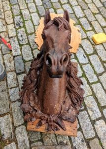 This is an old French cast iron horse head, most likely from the late 19th century. The patina suggests it spent lots of time outdoors. These horse heads were often used as emblems outside butcher shops specializing in horseflesh. Some were also used on the exterior walls of saddleries, or in front of a farrier or livery stable.