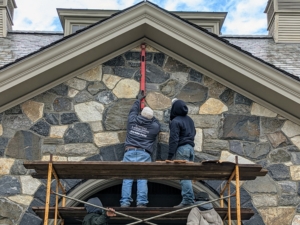 I knew I wanted the horse head to be above the center keystone of the doorway. A keystone is the wedge-shaped stone at the apex of a masonry arch. The keystone is the final piece placed during construction and locks all the stones into position, allowing the arch of the doorway to bear weight. Here, the crew uses a level to evaluate the surface of the stone where the horse head will be mounted.