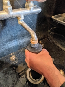 A thick tan rubber "priming button" is included with the replacement filters. It is is used to funnel water into the filter interior to saturate the media and flush out air and manufacturing dust. Carlos places the button on the filter and presses it against the faucet while the water runs slowly.