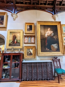 The walls of the gallery are filled with gilt-framed paintings.