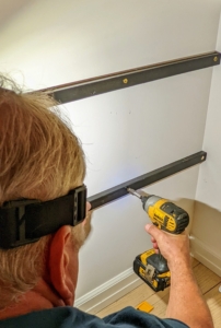He fastens two other battens on the other side with regular screws into the wall studs.