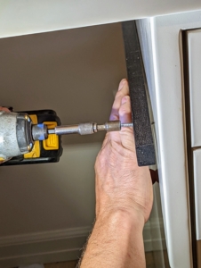 Doug fastens the self-drilling screw through the batten to secure it to the metal cabinetry behind it.