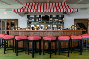 Not far is the Pridwin's Crescent Bar with its whimsical red, white and pink cabana stripe awning and bar stools upholstered in a warm pink fabric. The renovation project's design was under the direction of Colleen Bashaw, Curtis' sister and VP of design for Cape Resorts. She says "The Pridwin was based upon the hotel’s image of classic Adirondack summer camps and cottages" - a playful mix of old and new. (Photo courtesy of Cape Resorts)
