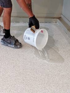 Next, he pours generous amounts of polyurea clear coat and sealer in the middle of the floor.