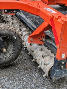 Here is a closer look at the roller of the power rake. When it is lowered onto the road surface and tilted to the proper angle, this attachment moves the gravel and road dust to the center, creating the proper crown for the surface. There should be about a three-percent slope from the shoulder to the center of the road.