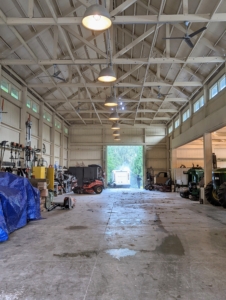 Here is a view of the inside. To clean it thoroughly, everything is brought out, the floor is cleaned and then everything is returned to its proper place. At night, this barn accommodates all our farm vehicles. Above, the space is well lit with these big overhead lamps. I use very utilitarian lighting and fans wherever I can.