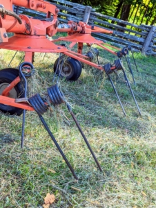 The tedder uses a rotary motion to grab the hay with spinning tines and then casts it out the back of the machine. Here is a closer look at the tines, or moving forks, which aerate or “wuffle” the hay and speed up the drying process.