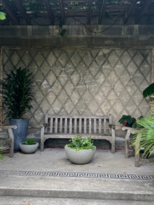 This is a stoa, a covered portico or walkway according to Greek architecture. It is embellished with a group of potted tropical specimens including a container planted with various ferns: emionitis arifolia, Selaginella, Impatiens repens, Pteris cretica ‘Albolineata,’ Pteris ensiformis ‘Evergemiensis,’ and Pellaea rotundifolia.