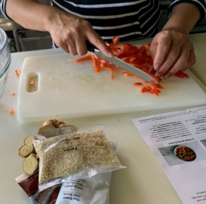 For this recipe, the first step is to prep all the ingredients. We call this part of the process "mise en place," a French term for having all the ingredients cut, peeled, sliced, grated, etc. before cooking. Here, Elvira cuts the red pepper into thin strips and then cuts the strips in half crosswise.
