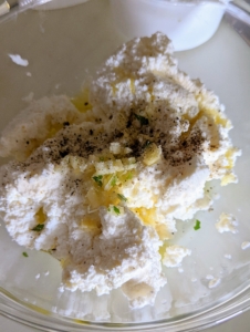 In a small bowl, she combines the ricotta, olive oil, and half of the chopped garlic along with some salt and pepper.
