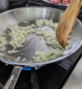 The next step is to start cooking the filling for the taquitos. Enma heats a tablespoon of oil in a large skillet over a medium-high flame and adds all but 1/4 cup of the chopped onions.