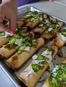 Finally, she tops the warm taquitos with the tomatilla salsa, sour cream, remaining onions, cilantro, and the sliced jalapeños - nothing is wasted.