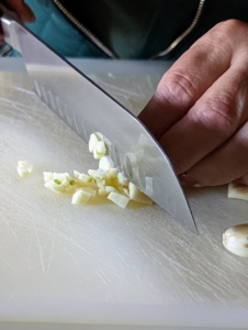 To start, while the oven is preheating to 450-degrees Fahrenheit, Enma prepares the ingredients for cooking. Here she is finely chopping two teaspoons of garlic, which is about two medium cloves.
