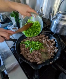 The meat is cooked through until lightly browned and then seasoned with salt and ground black pepper before Enma adds the green peppers, onions, and half the chopped garlic. After six to eight minutes, she adds some taco seasoning, also provided, some water, stirs and then removes it from the skillet to cool slightly.
