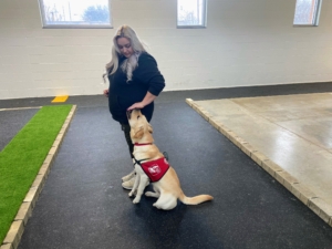 Trainer Megan Marie and Pilot Puppy Calvin are working on the "heel" command in the flight simulator, Pilot Dogs indoor training facility. The flight simulator is set up with a "city" feel, complete with curbs, fire hydrants, tree branches, and lots of other distractions to aid in training. (Photo courtesy of Pilot Dogs)