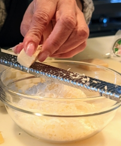 Next, Elvira finely grates all the Parmesan cheese using a long stainless steel grater.