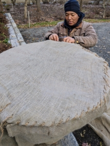 Once the burlap is secured and the ends are tucked and sewn, Phurba begins stitching the fabric together and pulling the burlap snug at the top and around the pot.