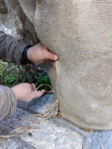 Starting from the bottom, Phurba makes small stitches and knots to keep the burlap in place. He also makes sure the burlap protects as much of the bottom as possible.