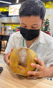 그들의 첫 번째 구매 중 하나는 신선한 코코넛 주스입니다.  여기에 밍마르는 안전하게 마실 수 있도록 마스크에 구멍을 뚫었다.